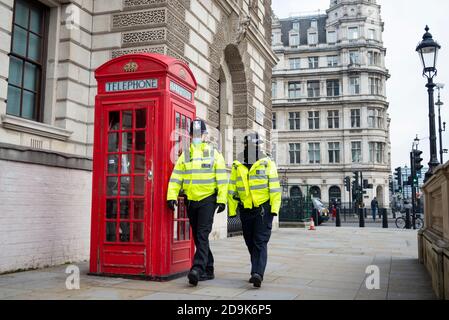 Polizeibeamte patrouillieren den Schlag in London, Großbritannien, am ersten Tag der zweiten nationalen Sperre COVID-19, vorbei an einer roten Telefondose. Protest fällig Stockfoto