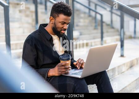 Junge attraktive amerikanische Geschäftsmann sitzt auf Treppen vor Riesiges, modernes Gebäude und ein paar Arbeiten an einem Laptop Stockfoto