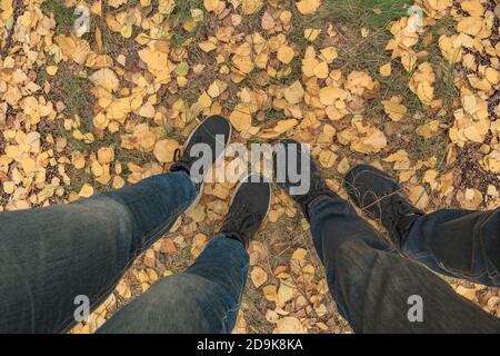 Männliche und weibliche Füße stehen auf den gelben Herbstblättern. Damenbeine. Ein junges Paar in Stiefeln steht im Wald. Menschen in Schuhen sind sta Stockfoto