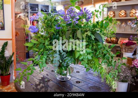 Blumenarrangement mit violetten Blumen, grünen Blättern und Eukalyptus auf Holztisch Stockfoto