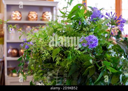 Blumenarrangement mit violetten Blumen, grünen Blättern und Eukalyptus auf Holztisch Stockfoto