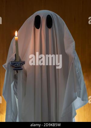 Ein Geist, der mit einem weißen Blatt bedeckt ist, geht mit einem Kerze in der Hand Stockfoto