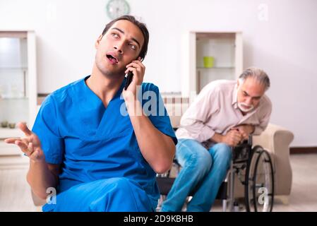 Alter Mann im Rollstuhl und schlechter Betreuer drinnen Stockfoto