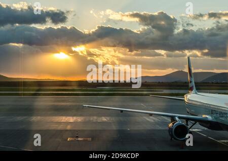 Flugzeug auf Athens Airport Airway mit einem wunderschönen Sonnenuntergang im Hintergrund. Orangefarbenes Sonnenlicht durch die Wolken am Himmel. Stockfoto