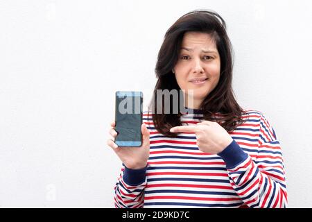 Portrait junge Frau hält Handy und zeigt auf den Bildschirm Stockfoto