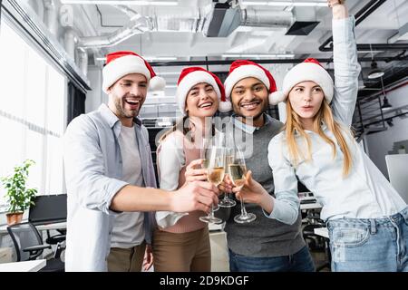 Positive multiethnische Geschäftsleute in santa Hüte mit Champagner in klimpern Büro Stockfoto