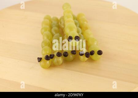 Spaß Party Essen für Kinder. Trauben und vegane Schokoladenstückchen arrangieren sich wie Schlangen, Stockfoto