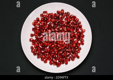 Granatapfelkerne auf einem Teller isoliert auf schwarzem Hintergrund. Frisch geschälter Granatapfel. Gesunde gesunde Ernährung mit Vitaminen Stockfoto
