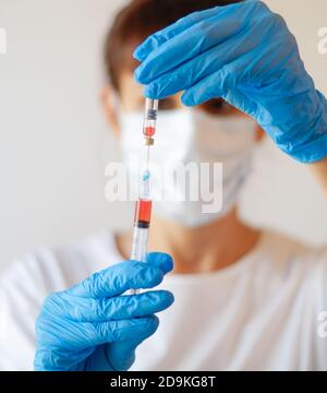 Arzt Krankenschwester Frau trägt Schutzmaske und Handschuhe - hält Virus Blut Teströhrchen und Spritze Stockfoto