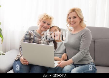 Glückliche drei Generationen von Frauen sitzen entspannen auf der Couch Lachen beobachten lustige Video auf Laptop, lächelnd positive Frauen Großmutter, Mutter und Tochter Stockfoto