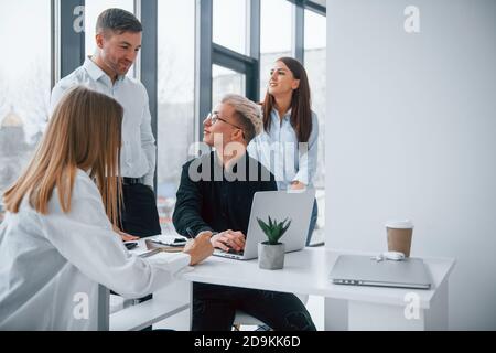 Positives junges Team, das mit Laptop arbeitet und in Innenräumen miteinander kommuniziert Im Büro Stockfoto