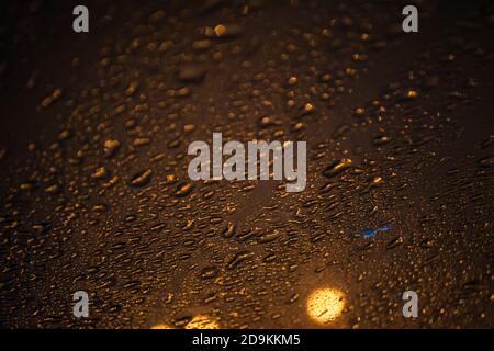 Natürliche Wassertropfen auf Glas, Nachtfoto mit Straßenlaternen draußen. Hintergrund aus Tropfen, selektiver Fokus, Ort für Text Stockfoto