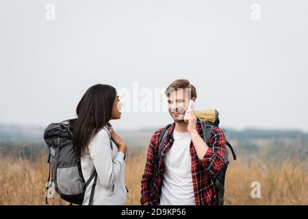 afroamerikanische Frau mit Rucksack in der Nähe von Freund im Gespräch Smartphone im Freien während der Reise Stockfoto