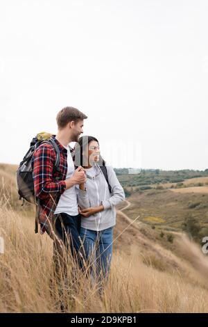 Lächelnd interracial paar Touristen halten Hände, während im Stehen Gras auf dem Hügel Stockfoto