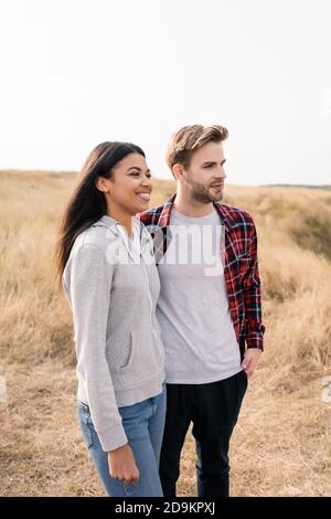 Lächelnde afroamerikanische Frau, die in der Nähe von Freund auf Rasen im Freien steht Stockfoto