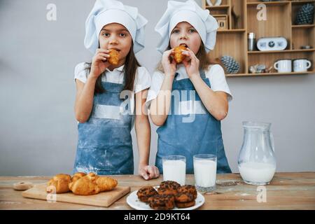 Zwei kleine Mädchen in blauer Chefuniform essen Essen auf Die Küche Stockfoto