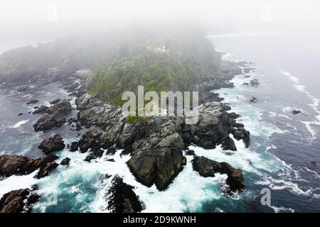 Atemberaubende Luftaufnahme von steilen Klippen und Leuchtturm auf der Spitze des Hügels. Drone Blick von oben auf zerklüftete felsige Küste. Gefahr Meereswellen krachen Stockfoto