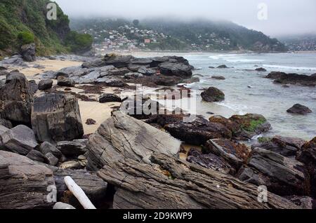 Riesige Felsen an einem Meeresstrand. Neblig bewölktes Wetter. Kleines Dorf auf einem Hügel im Hintergrund. Maicolpue, Osorno, Pazifikküste, Chile. Stockfoto