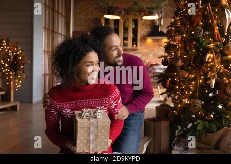 Verträumt lächelndes afroamerikanisches Paar umarmt, Weihnachtswünsche machend Stockfoto