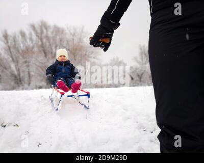 Kindheit, Rodeln, Freizeitaktivitäten Konzept. Eltern, die gerne kleine Kind auf Schlitten im Winter Stockfoto