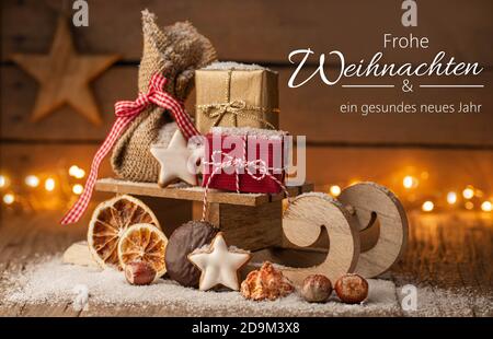 Weihnachtsgrüße in deutscher Sprache - kleiner Schlitten mit Geschenken und Lichter auf Holz Stockfoto