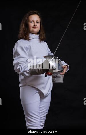 Teenager-Mädchen Fencer in Uniform mit epee und Helm gekleidet studio Porträt auf schwarzem Hintergrund Stockfoto