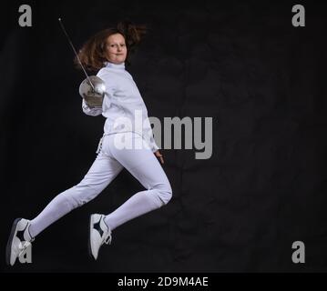 Teenager-Mädchen Fencer in Uniform mit epee und Helm gekleidet studio Porträt auf schwarzem Hintergrund Stockfoto