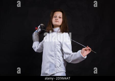 Teenager-Mädchen Fencer in Uniform mit epee und Helm gekleidet studio Porträt auf schwarzem Hintergrund Stockfoto