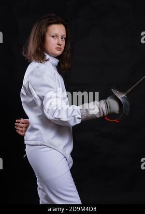 Teenager-Mädchen Fencer in Uniform mit epee und Helm gekleidet studio Porträt auf schwarzem Hintergrund Stockfoto