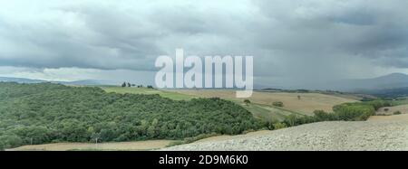 Stürmischer Himmel über der grünen hügeligen toskanischen Landschaft, aufgenommen in hellem Licht in der Nähe von San Quirico, Siena, Toskana, Italien Stockfoto