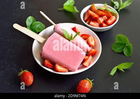 Erdbeer-Eis-Eiszapfen auf weißem Teller auf dunklem Steingrund. Stockfoto