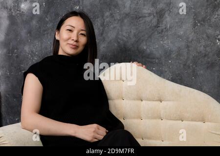 Schöne koreanische Frau in schwarzem Kleid auf dem Sofa sitzend gekleidet studio-Porträt Stockfoto