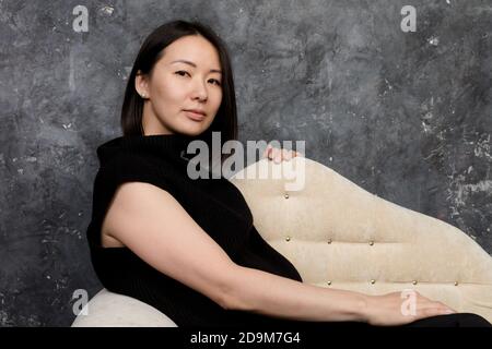 Schöne koreanische Frau in schwarzem Kleid auf dem Sofa sitzend gekleidet studio-Porträt Stockfoto