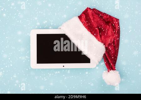 Weihnachtskonzept Hintergrund.Digitale Tablette in weihnachtsmann Hut mit Schneeflocken Auf blauem Hintergrund Stockfoto