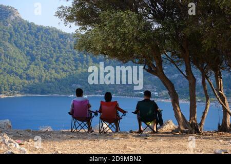 Die Leute sitzen auf Stühlen und genießen den Blick auf den Kumlubuk Strand und das Meer in der Nähe von Marmaris, Türkei Stockfoto