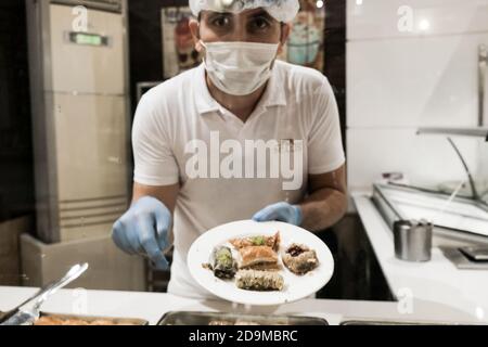 Belek, Türkei - Oktober 2020: Mann mit Gesichtsmaske und Handschuhen, der türkischen Baklava für Touristen im All-Inclusive-Hotel in der Türkei serviert. Köstlich traditionell Stockfoto