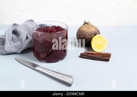 Rübenkonfitüre in einem Glas mit Rüben, Zitronen- und Zimtstangen auf grauem Hintergrund. Vegetarismus-Konzept. Speicherplatz kopieren. Selektiver Fokus. Stockfoto