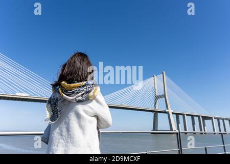 Rückansicht einer Frau, die am Flussufer steht und auf den Fluss blickt Brücke Stockfoto