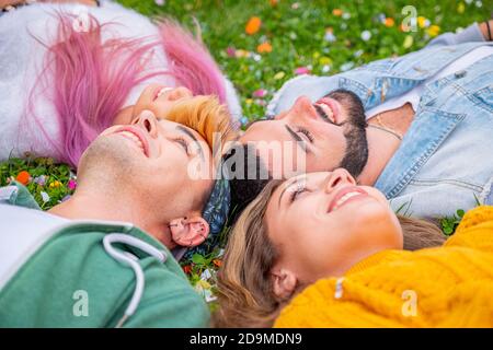 Gruppe lächelnder Freunde, die auf dem Gras liegen und gefärbt sind Konfetti im Freien - Draufsicht auf schöne stilvolle Freunde suchen Bei der Kamera im Kreis und s Stockfoto