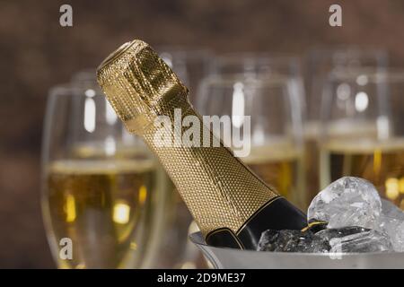 Close up of a champagne bottle neck with ice cubes with out of focus champagne glasses at the back Stockfoto
