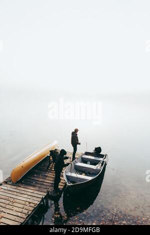 Mann und Kind machen sich bereit, an einem nebligen Tag in einem Boot angeln zu gehen. Stockfoto