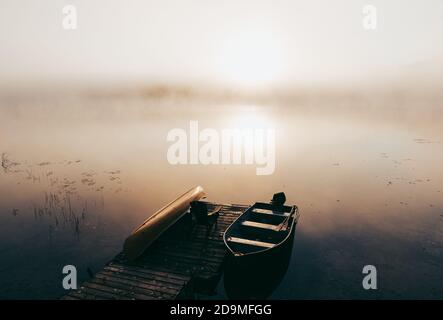Leeres Dock mit festgebundenen Booten an einem nebligen Morgen auf einem ruhigen See. Stockfoto