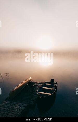 Leeres Dock mit festgebundenen Booten an einem nebligen Morgen auf einem ruhigen See. Stockfoto