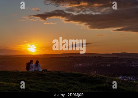 Zwei Leute sitzen auf dem Burghügel und beobachten die Sonne Über West Yorkshire gelegen Stockfoto