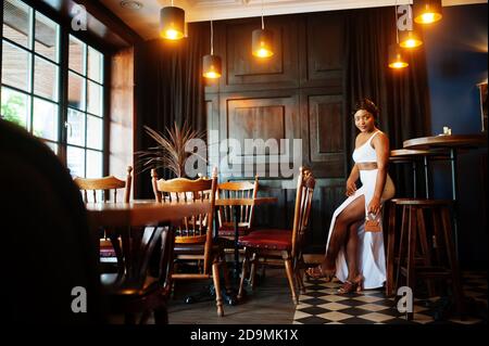 afroamerikanische Frau, Retro-Frisur in weißem Kleid im Restaurant. Stockfoto