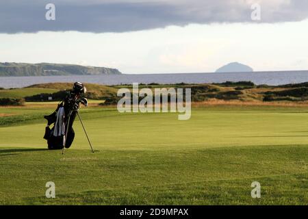 Golfplatz St. Ninnians, Prestwick, Ayrshire, Schottland, Großbritannien. Eine Golftasche sitzt am Rand des Grüns. Im Bckground befindet sich die ikonische Form von Ailsa Craig an der Westküste Schottlands, Stockfoto