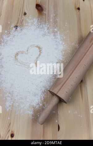 Das Nudelholz und das weiße Mehl verschüttet auf dem hölzernen Tisch und die Zeichnung des Herzens. Liebe zum Backen Konzept. Valentinstag Backen Süßigkeiten Stockfoto