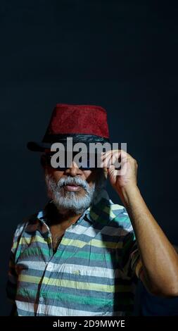 Porträt eines bärtigen asiatischen älteren Mannes mit Hut Und Sonnenbrillen isoliert auf schwarzem Hintergrund Stockfoto