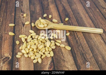 Pinienkerne in einem Holzlöffel und auf a verstreut Holztisch Stockfoto