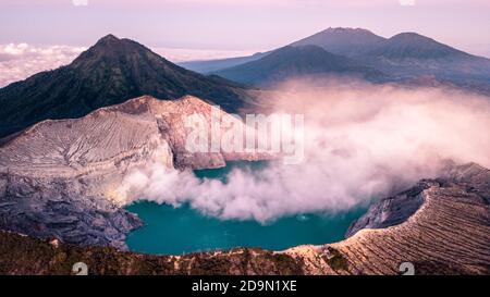 Kawah Ijen von oben mit dampfenden Schwefelfedern und einer Saurer See mit einer kleinen Eruption Stockfoto